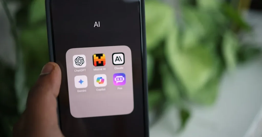 Hand holding a smartphone showing an &ldquo;AI&rdquo; folder with ChatGPT and other AI app icons, set against blurred green foliage; modern, tech-focused mood.